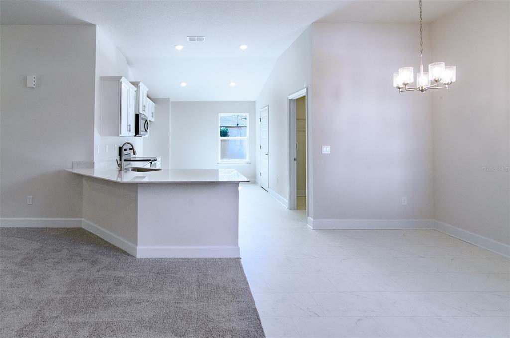 A kitchen with white cabinets and a breakfast bar overlooks a carpeted living area — 14 WENDOVER LANE, PALM COAST, FL