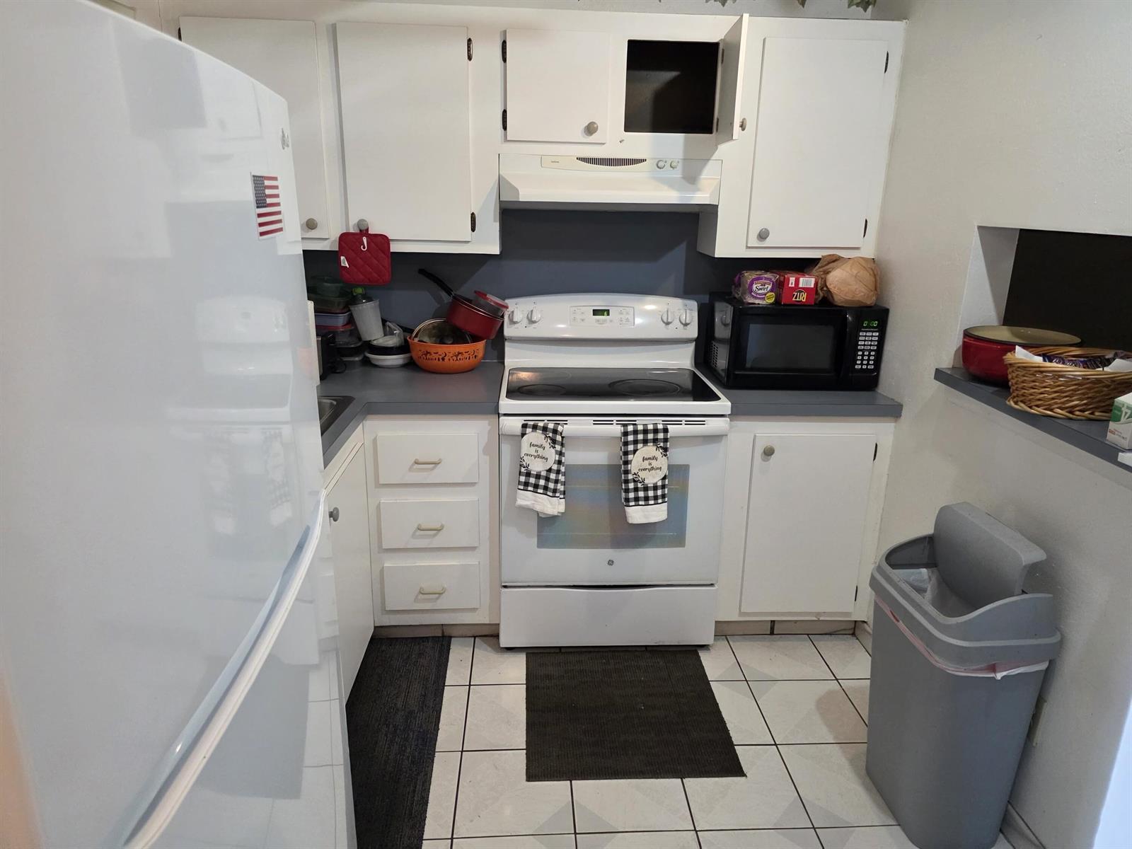 A small kitchen features white cabinets, a white stove, a microwave, and tiled flooring — 3048 E Sunrise Lakes Drive E # 412, Sunrise FL 33322, SUNRISE, FL