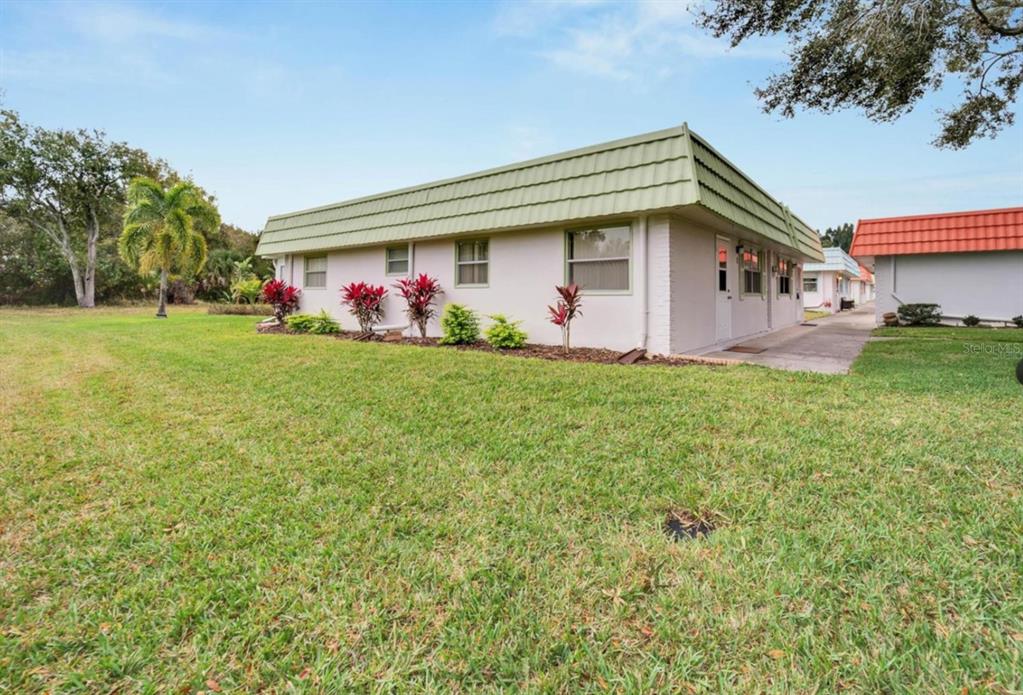 A single-story building with a green mansard roof and light-colored walls sits on grass — 1802 BEDFORD LANE UNIT 1, SUN CITY CENTER, FL