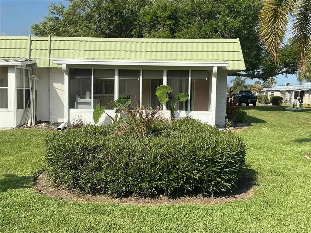 A white house with a green metal roof features a screened-in porch and landscaping — 1802 BEDFORD LANE UNIT 1, SUN CITY CENTER, FL