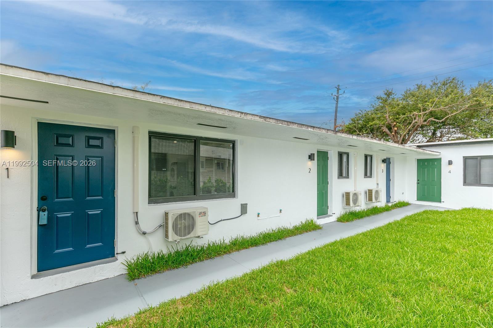 The exterior of a white apartment building features numbered doors and individual wall-mounted air conditioners — 6125 SW 40th Ct, Miramar FL 33023, MIRAMAR, FL