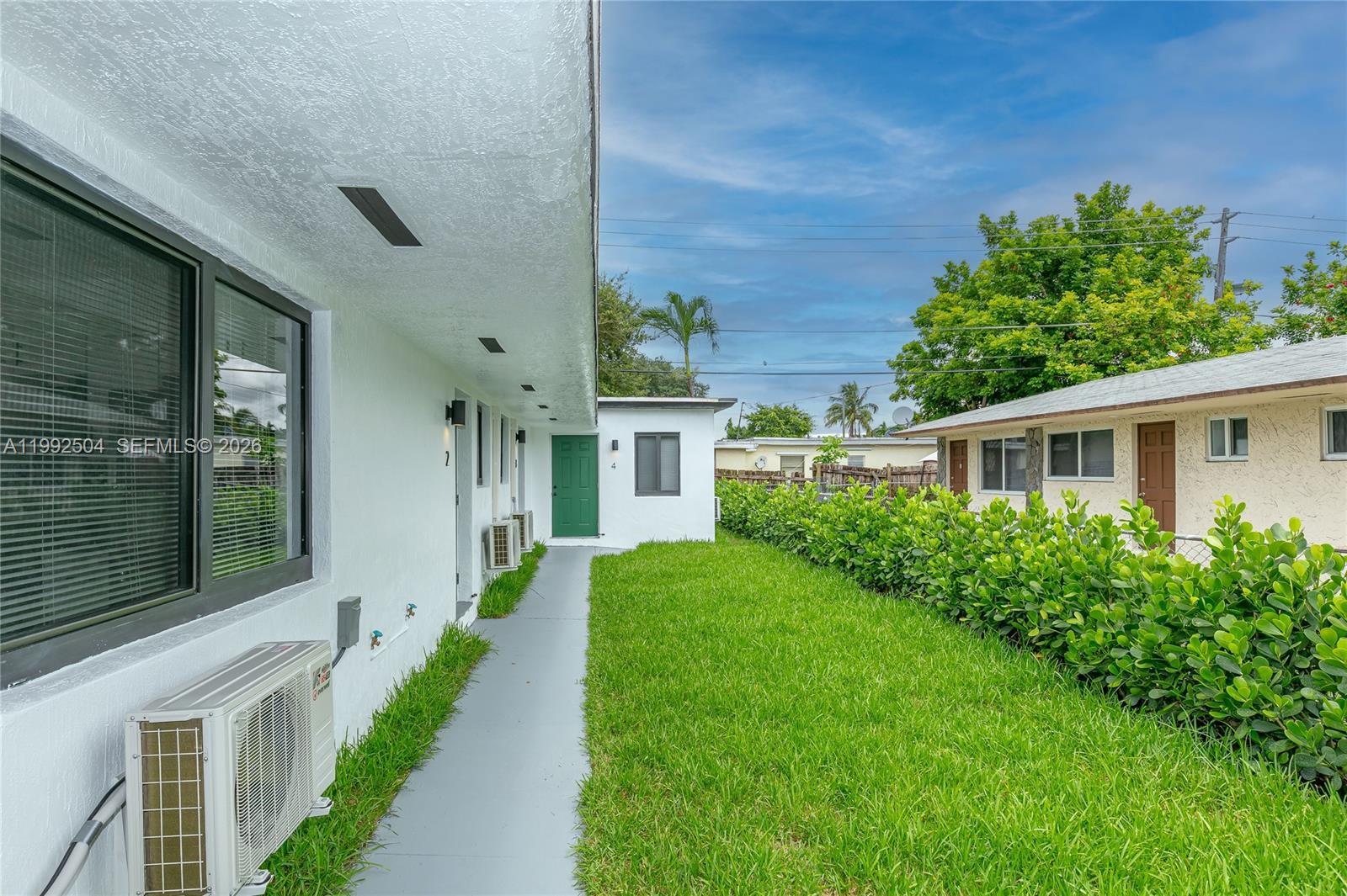 A white building exterior features a green door, a gray walkway, and a grassy lawn — 6125 SW 40th Ct, Miramar FL 33023, MIRAMAR, FL