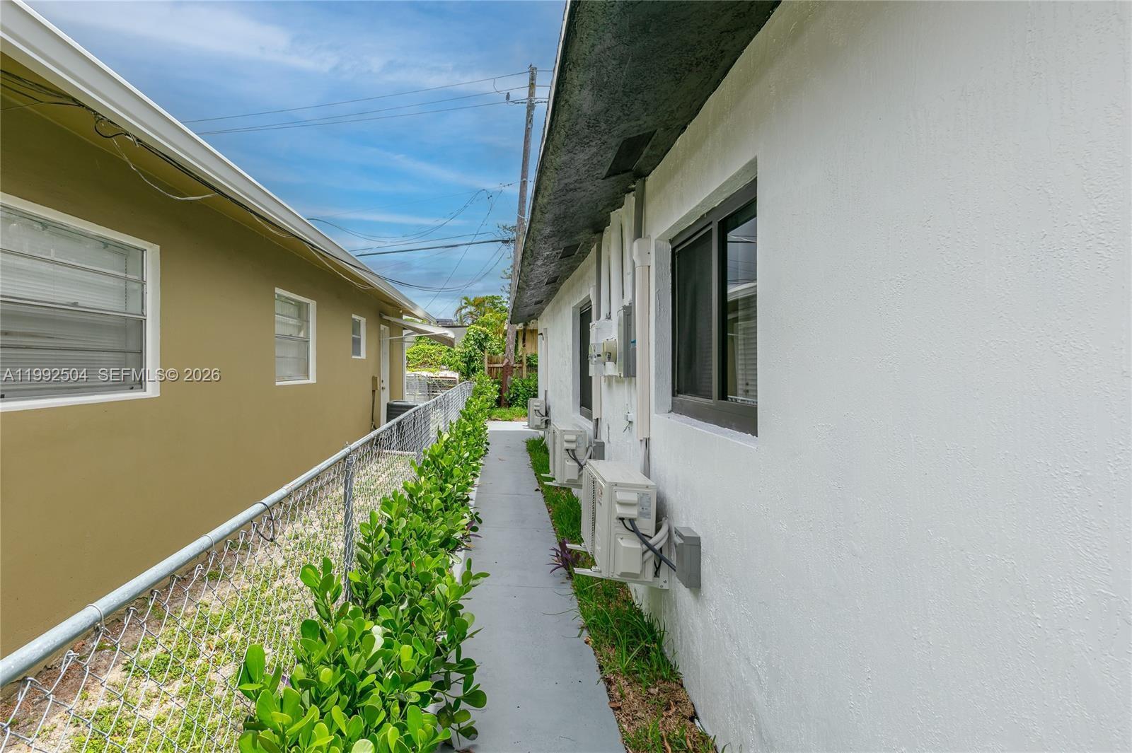 A narrow concrete walkway separates two residential buildings with exterior air conditioning units — 6125 SW 40th Ct, Miramar FL 33023, MIRAMAR, FL