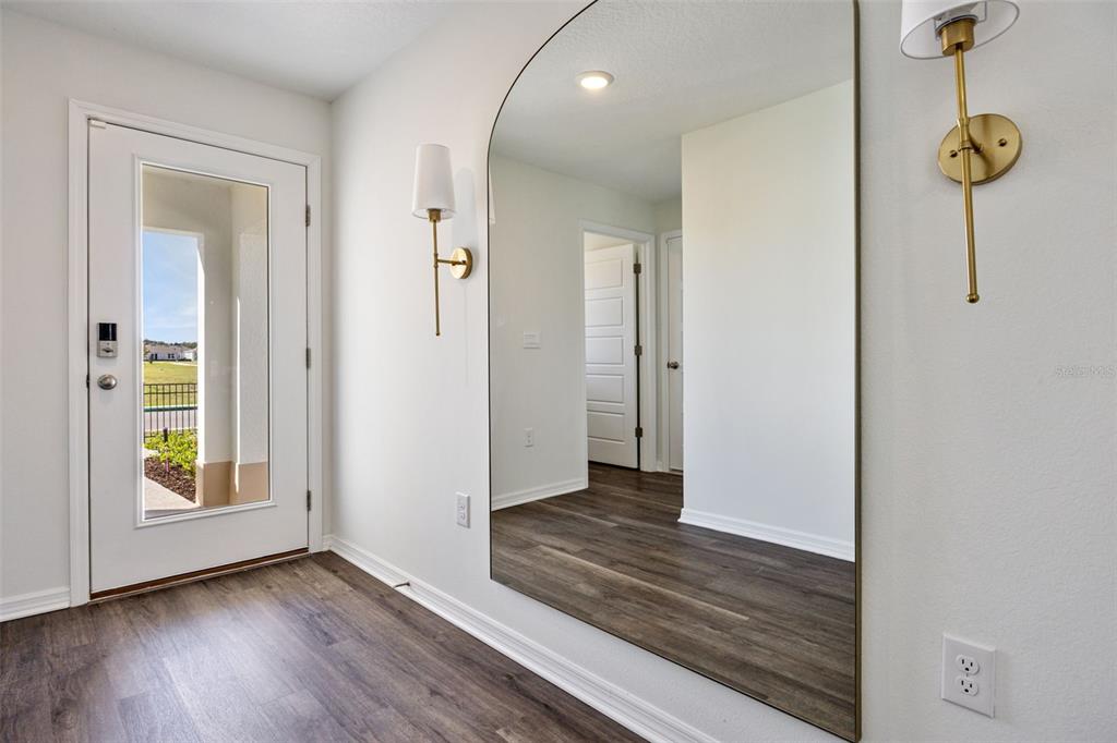 An entryway features wood-look flooring, a large arched mirror, and two brass wall sconces — 4222 BIXBY BRIDGE PLACE, DAVENPORT, FL