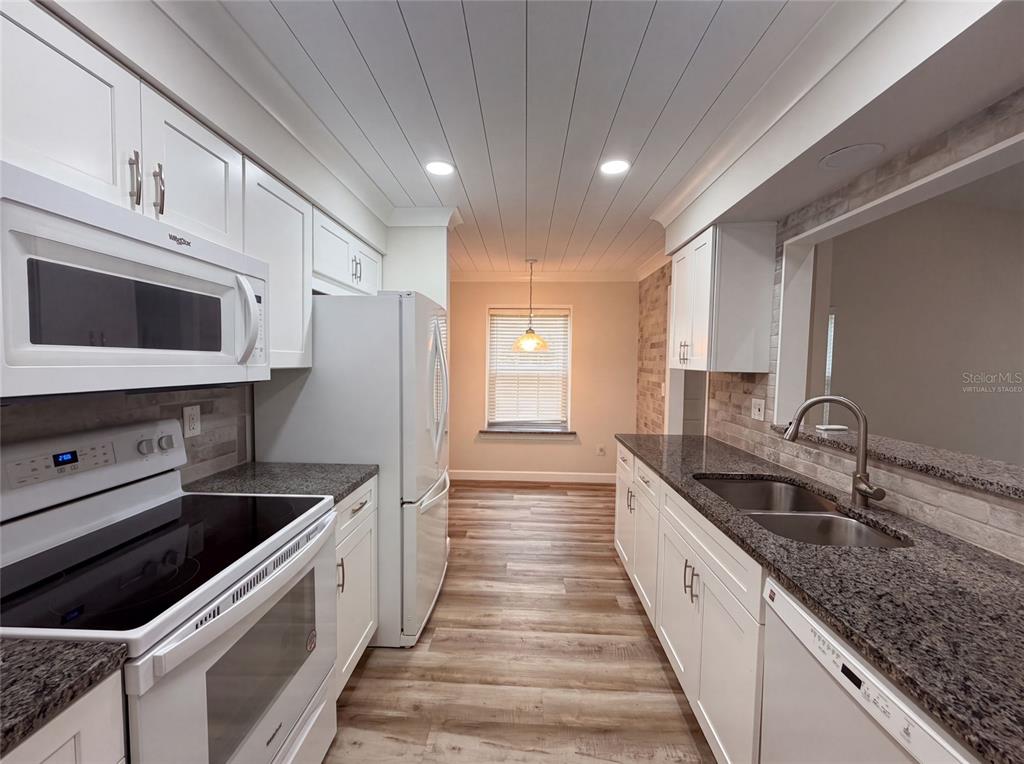A galley kitchen features white cabinets, granite countertops, stainless steel appliances, and wood-look flooring — 228 BOB WHITE COURT UNIT 2280, DAYTONA BEACH, FL