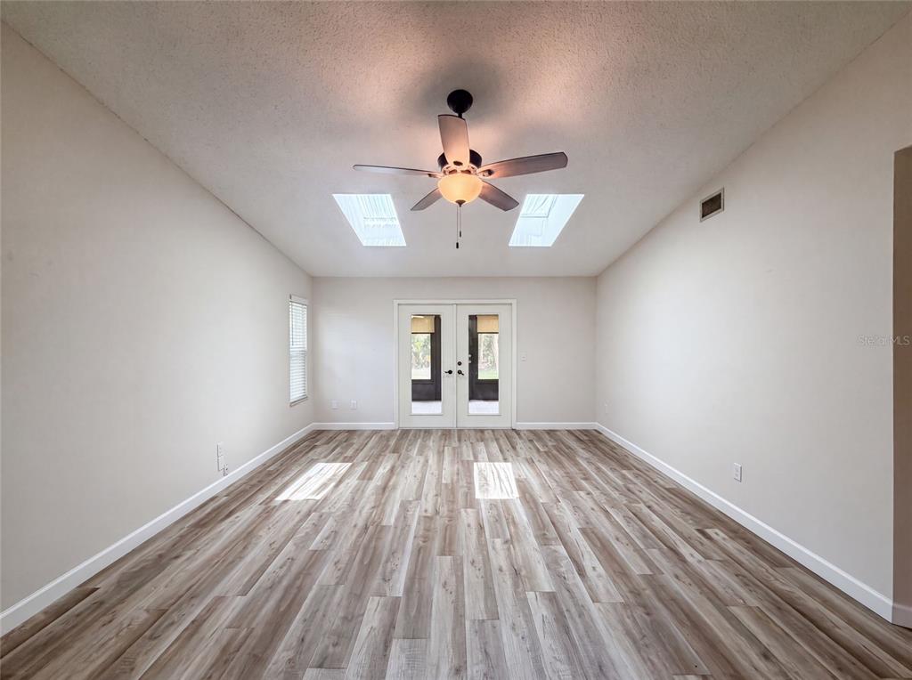 An empty room features wood-look flooring, a ceiling fan, two skylights, and double glass doors — 228 BOB WHITE COURT UNIT 2280, DAYTONA BEACH, FL