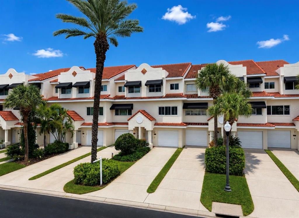 A row of multi-story townhouses with white stucco walls, red tile roofs, and attached garages — 4629 MIRABELLA COURT, ST PETE BEACH, FL