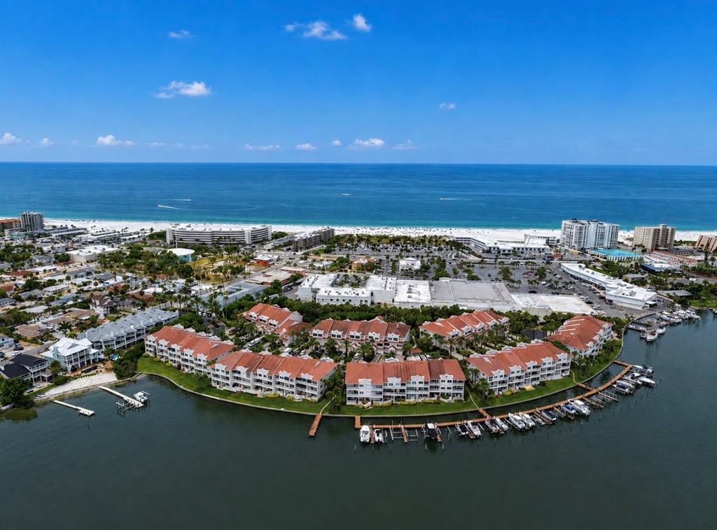 A living room with a floral sectional sofa, wood flooring, mirrored walls, and waterfront views — 4629 MIRABELLA COURT, ST PETE BEACH, FL