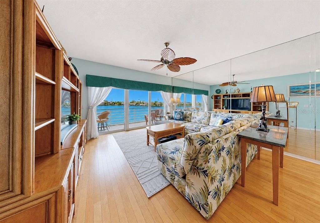 A living room features a large sectional sofa, hardwood floors, mirrored walls, and a staircase — 4629 MIRABELLA COURT, ST PETE BEACH, FL
