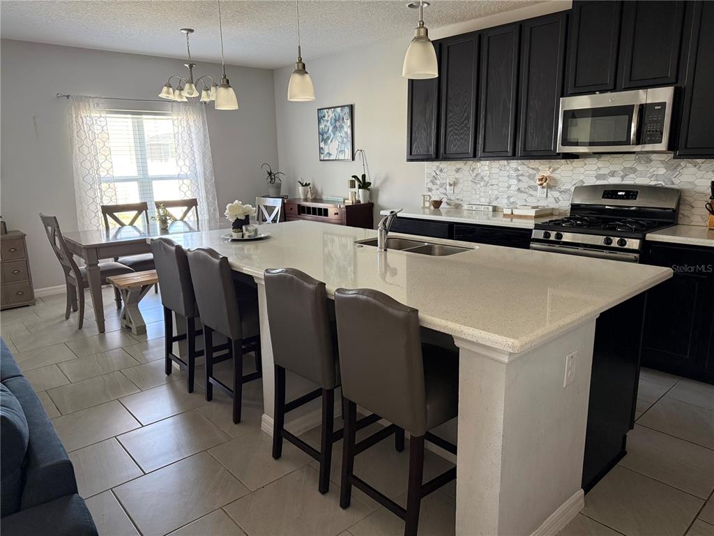 A kitchen features a large quartz island with bar seating, dark cabinets, and tile flooring — 1501 FINCHBURG STREET, MINNEOLA, FL