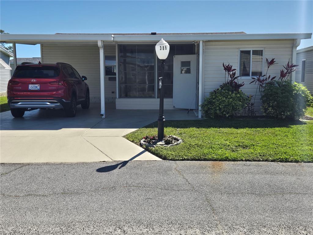 A single-story manufactured home features a carport with a red SUV and a front lawn — 386 TOWNBRIDGE DRIVE, HAINES CITY, FL