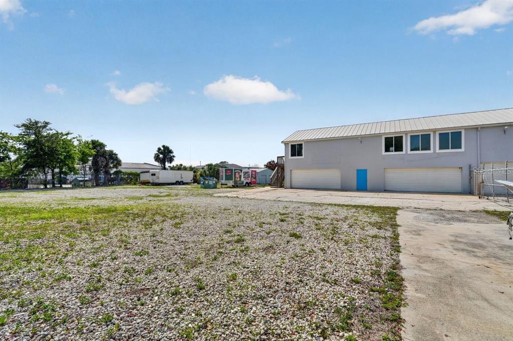 A gravel lot sits in front of a gray multi-story building with two garage doors — 468 RIDGEWOOD AVENUE, DAYTONA BEACH, FL