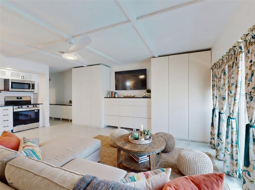 A living room with a kitchen, white cabinetry, a wall-mounted television, and a sectional sofa — 3700 S ATLANTIC AVENUE UNIT 207, NEW SMYRNA BEACH, FL