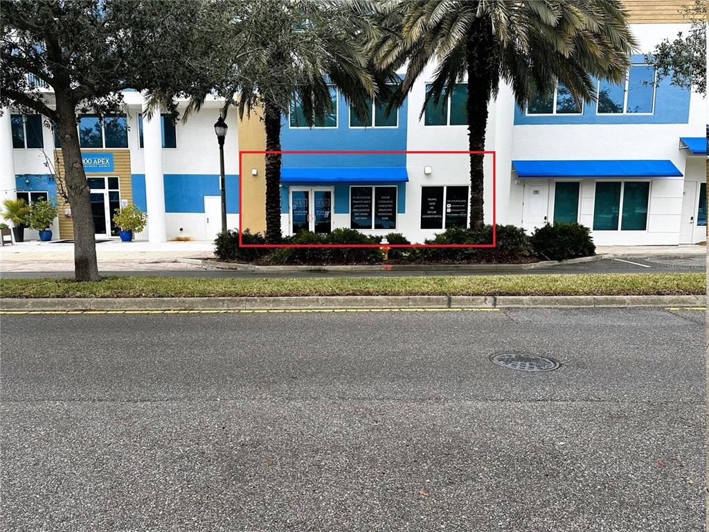 A commercial storefront with blue awnings and glass doors sits behind a landscaped median — 1100 CLEVELAND STREET, CLEARWATER, FL