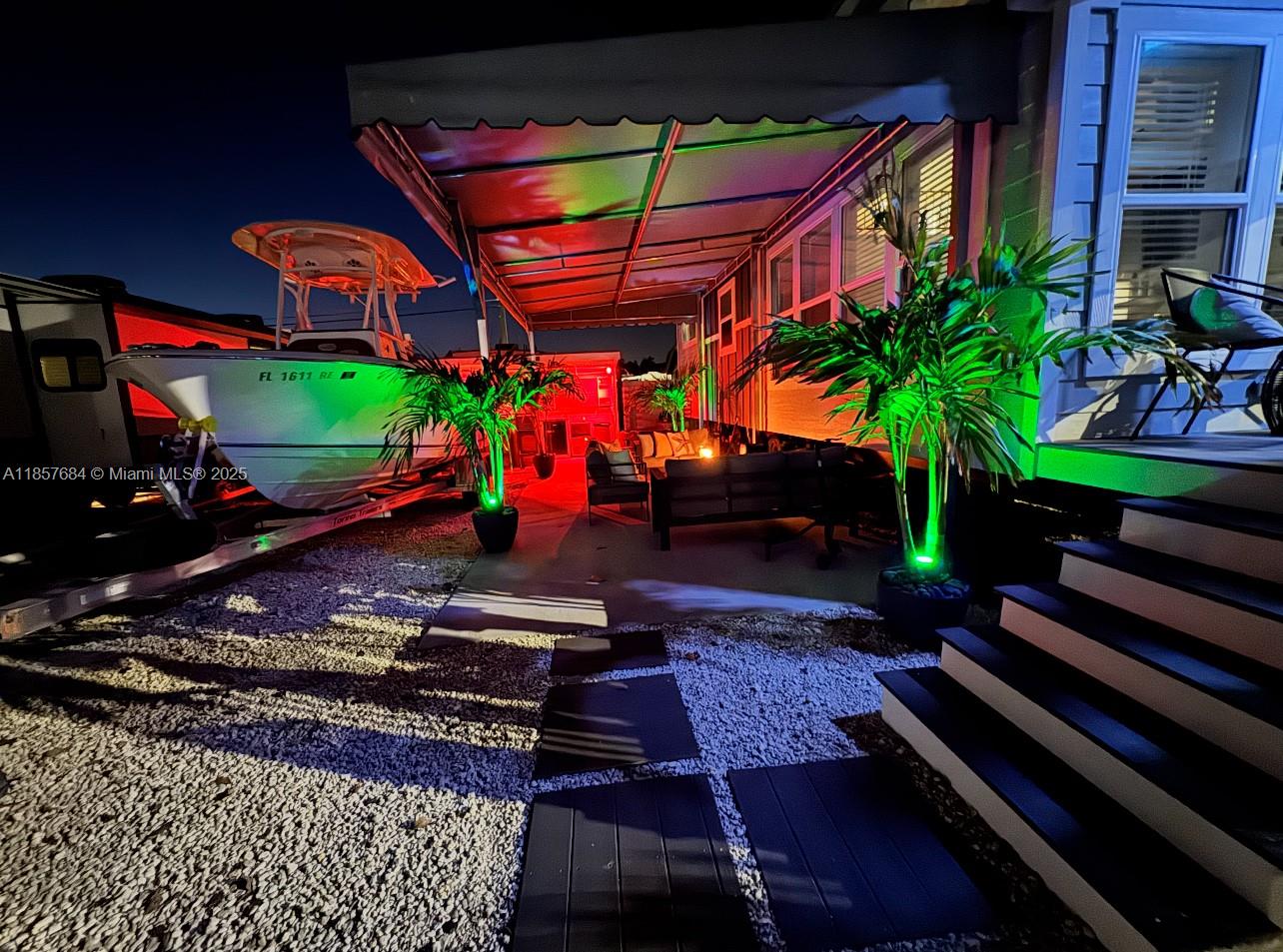 An outdoor patio area features a boat, potted palm trees, and colorful accent lighting at night — 325 Calusa St 302, Key Largo FL 33037, KEY LARGO, FL