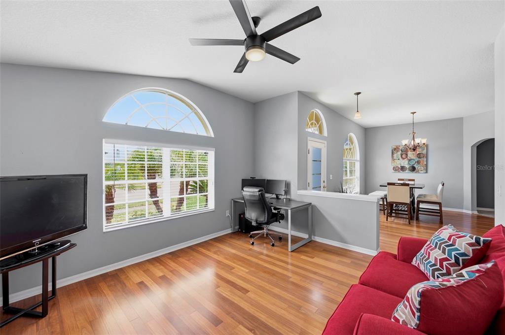 A living room with hardwood floors, a red sofa, a desk, and a dining area — 29609 EAGLE STATION DRIVE, WESLEY CHAPEL, FL