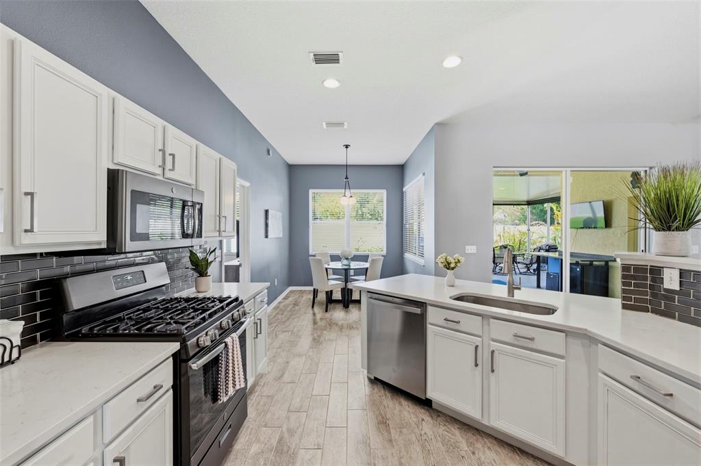 A modern kitchen with white cabinets, stainless steel appliances, and a dining area beyond — 29609 EAGLE STATION DRIVE, WESLEY CHAPEL, FL
