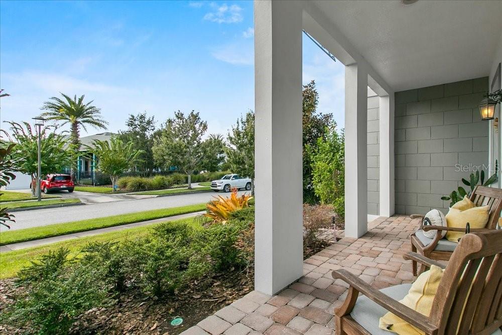 A covered front porch with paver flooring features two wooden chairs overlooking a suburban street — 14129 CORRIGAN AVENUE, ORLANDO, FL