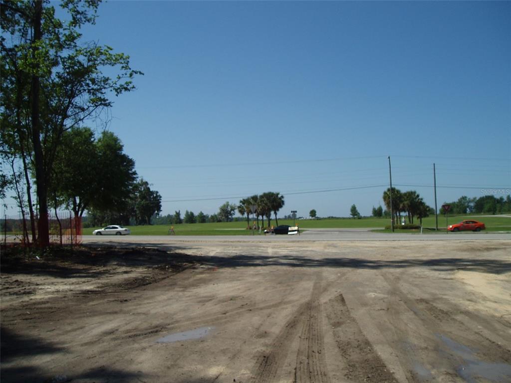 A dirt lot overlooks a paved road with trees, power lines, and passing cars — US HWY 441, ALACHUA, FL