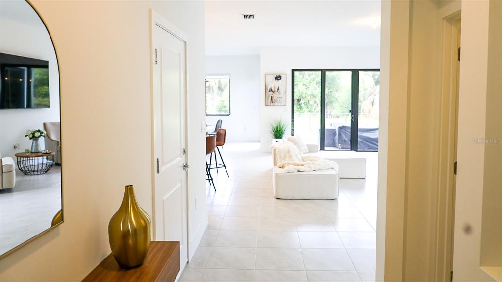 A bright, open-concept living area features white tile floors, a modern sofa, and a hallway — 5868 AGOSTINO WAY, AVE MARIA, FL