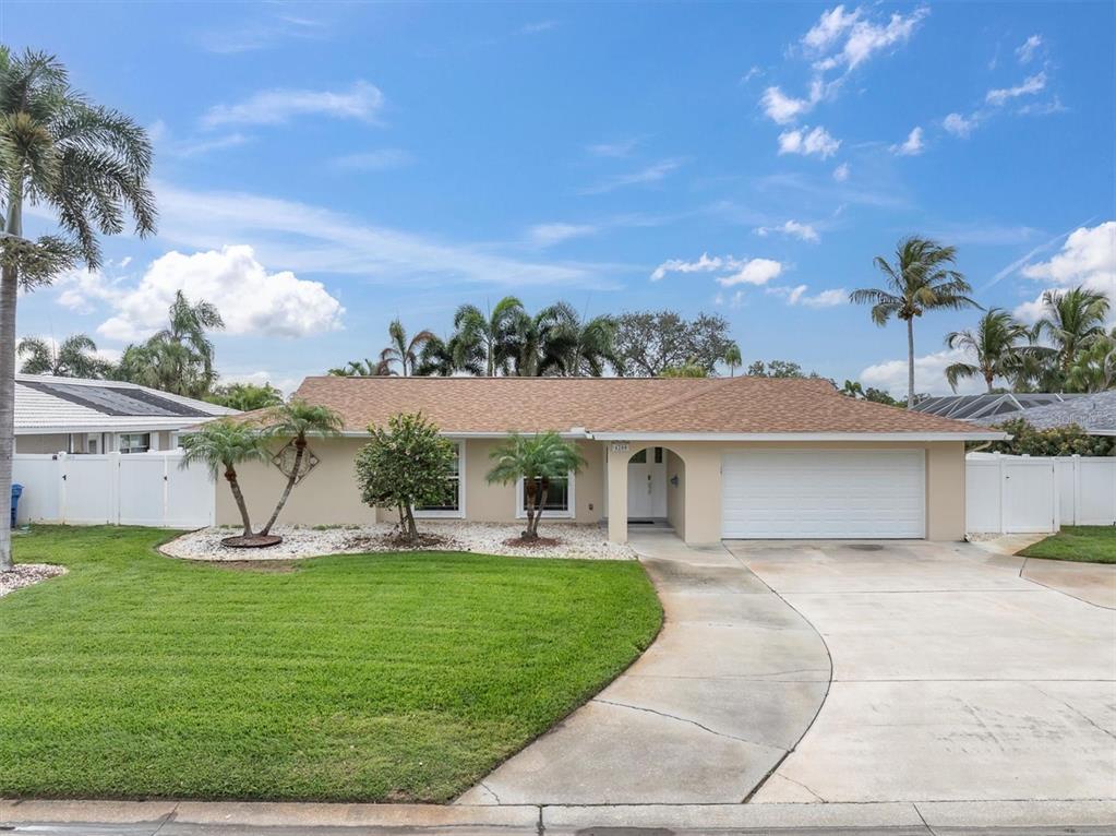 A single-story house with a tan exterior, brown roof, white garage door, and palm trees — 4200 46TH AVENUE S, ST PETERSBURG, FL