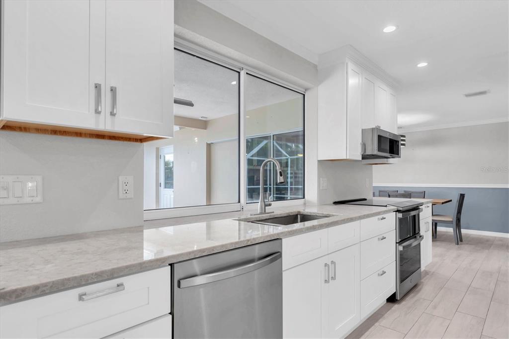 A modern kitchen features white cabinets, stainless steel appliances, and light-colored stone countertops — 4200 46TH AVENUE S, ST PETERSBURG, FL