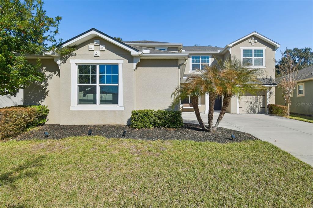 A two-story suburban house with a tan stucco exterior, a palm tree, and a driveway — 2604 VALLEY SUNSET LANE, VALRICO, FL