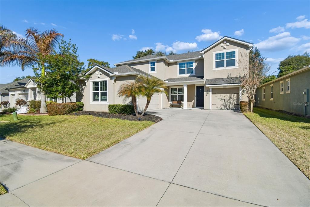 A two-story suburban house features a beige stucco exterior, a concrete driveway, and palm trees — 2604 VALLEY SUNSET LANE, VALRICO, FL