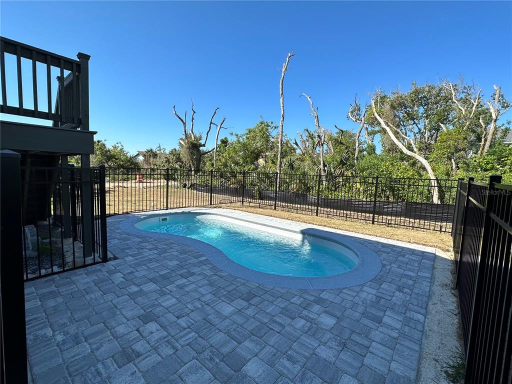 A small, kidney-shaped swimming pool sits on a paved patio enclosed by a black fence — 37 ATLANTIC DRIVE, PALM COAST, FL