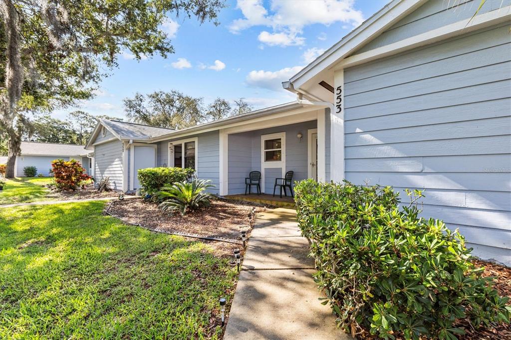 A light blue house exterior features a concrete walkway leading to a covered front porch — 39650 US HIGHWAY 19 N UNIT 553, TARPON SPRINGS, FL