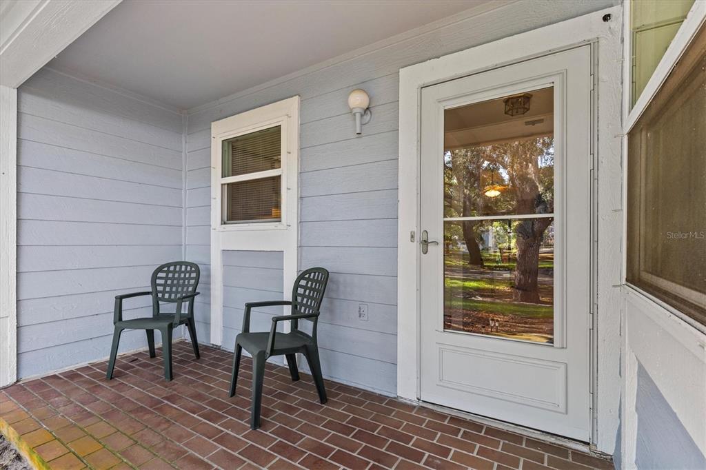 A covered porch features light blue siding, a brick floor, two chairs, and a door — 39650 US HIGHWAY 19 N UNIT 553, TARPON SPRINGS, FL