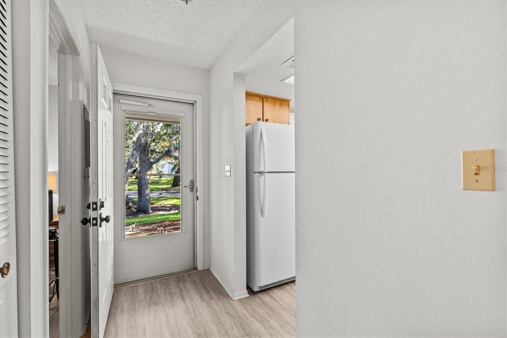 A view from a hallway toward a white door, a kitchen refrigerator, and outdoor trees — 39650 US HIGHWAY 19 N UNIT 553, TARPON SPRINGS, FL