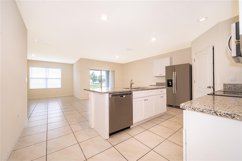 A kitchen with white cabinets, granite countertops, and stainless steel appliances opens to a living area — 5354 PALOMINO PLACE, APOPKA, FL