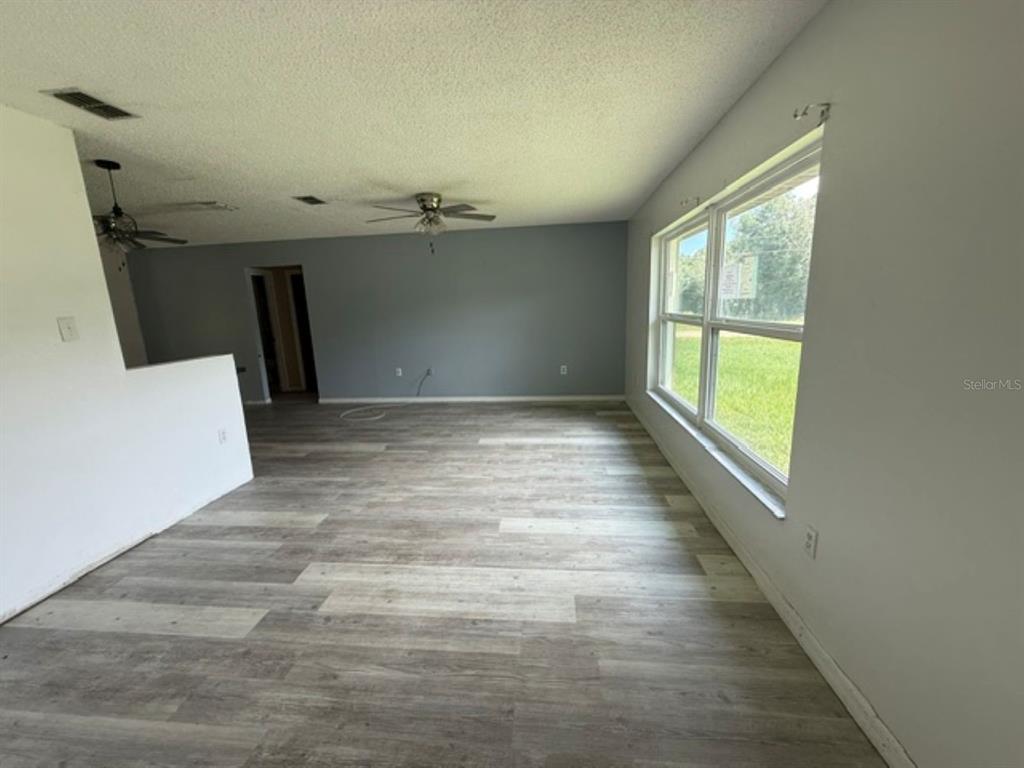 An empty living room features light wood-look flooring, gray walls, and a large window — 11160 SW 136TH COURT ROAD, DUNNELLON, FL