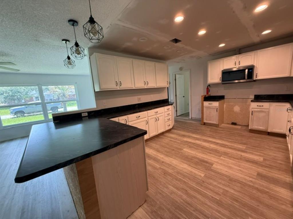 A kitchen features white cabinets, black countertops, wood-look flooring, and three hanging pendant lights — 11160 SW 136TH COURT ROAD, DUNNELLON, FL