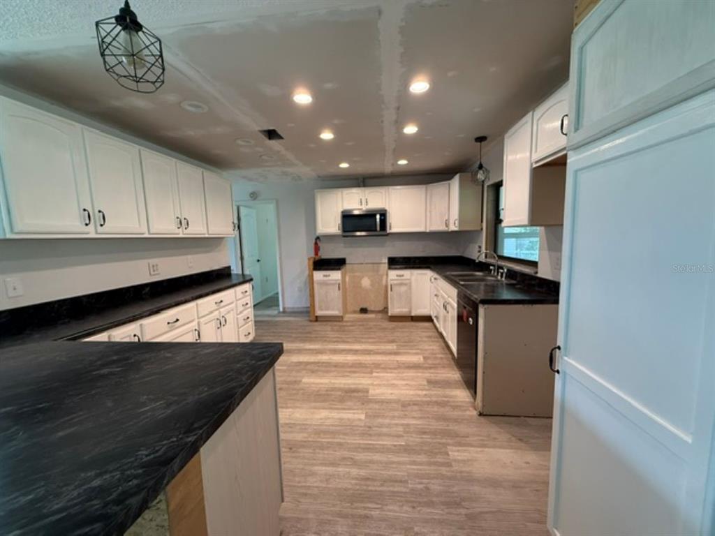 A kitchen features white cabinets, black countertops, recessed lighting, and light wood-look flooring — 11160 SW 136TH COURT ROAD, DUNNELLON, FL