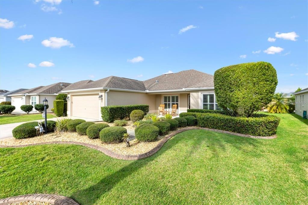 A single-story house with a tan exterior, a two-car garage, and manicured landscaping — 3394 RIDGEWOOD PATH, THE VILLAGES, FL