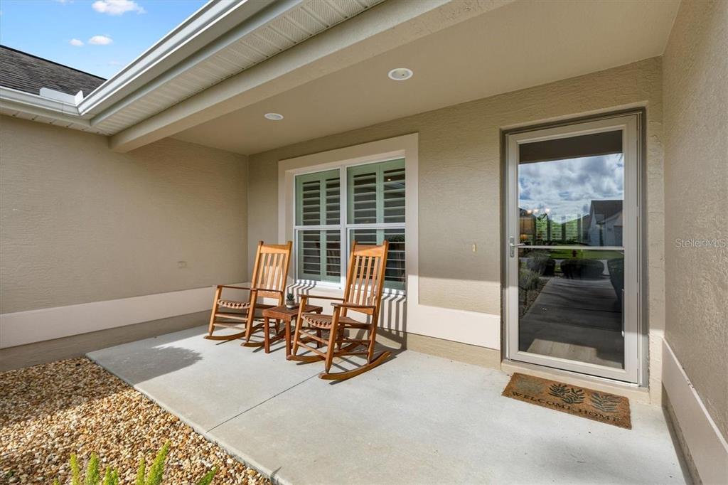 A covered concrete patio features two wooden rocking chairs and a glass storm door — 3394 RIDGEWOOD PATH, THE VILLAGES, FL