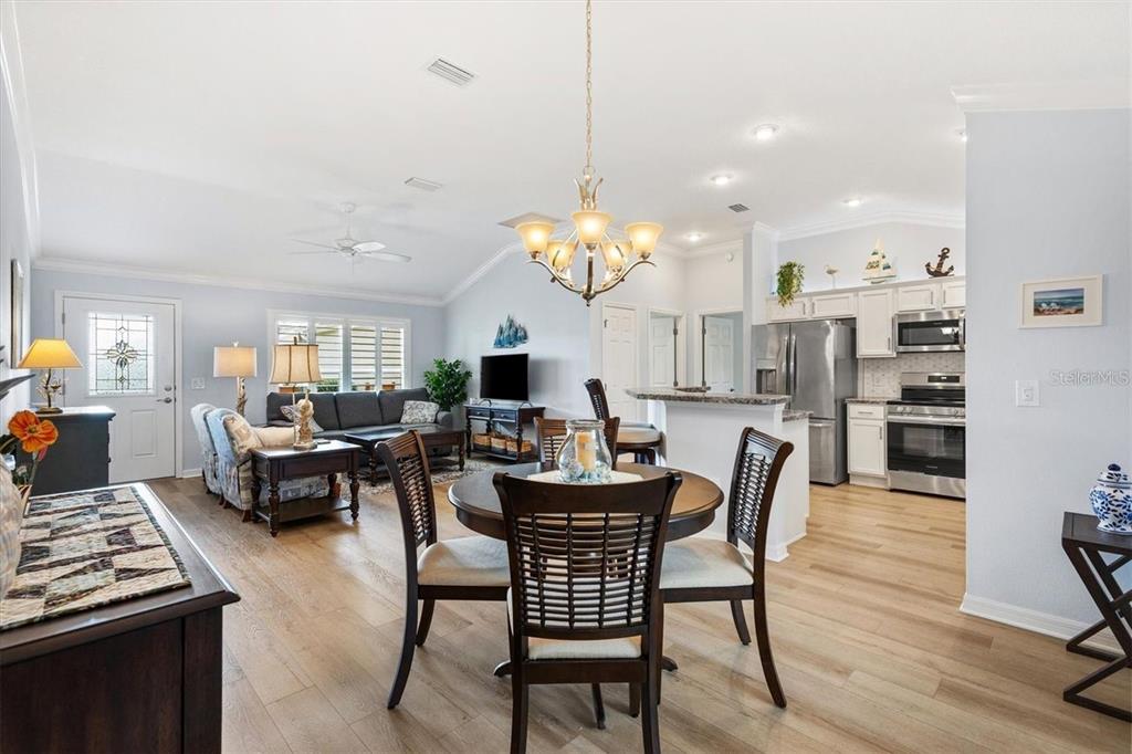 An open-concept living and dining area features light wood flooring, a chandelier, and a kitchen — 3394 RIDGEWOOD PATH, THE VILLAGES, FL