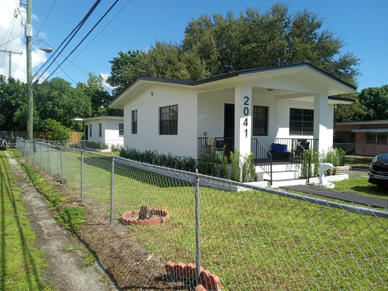 A white single-story house with a covered porch stands behind a chain-link fence — 2041 NW 100th St, Miami FL 33147, MIAMI, FL