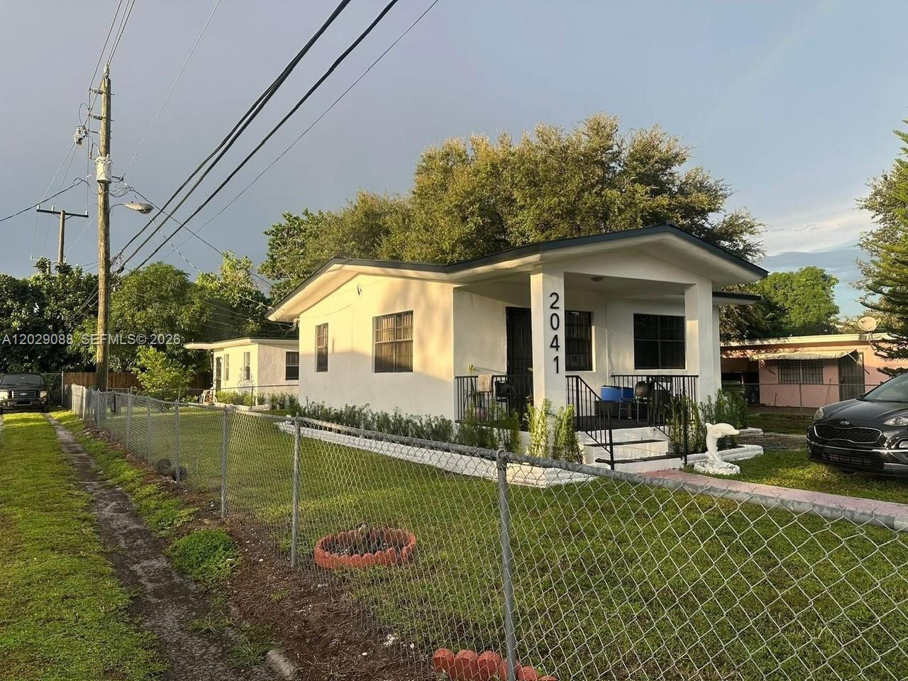 A white single-story house with a front porch and chain-link fence stands on a lawn — 2041 NW 100th St, Miami FL 33147, MIAMI, FL