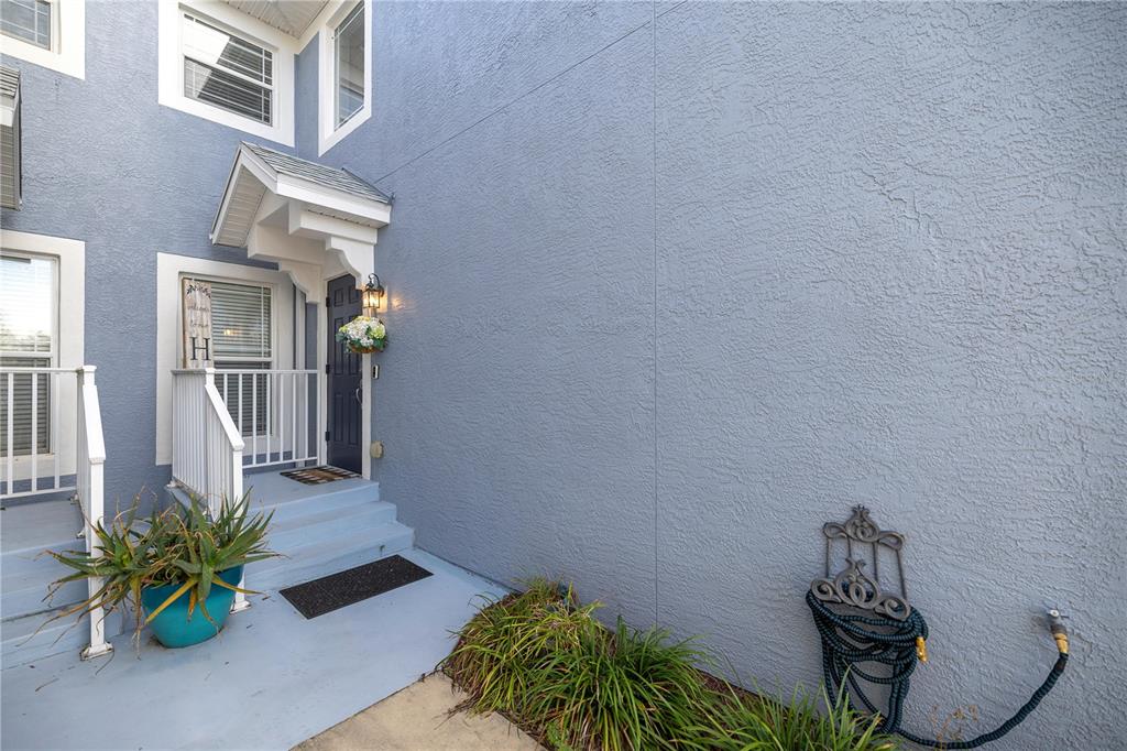 The exterior of a blue townhouse features a small covered entryway, stairs, and a hose — 4525 SW 52ND CIRCLE UNIT 106, OCALA, FL