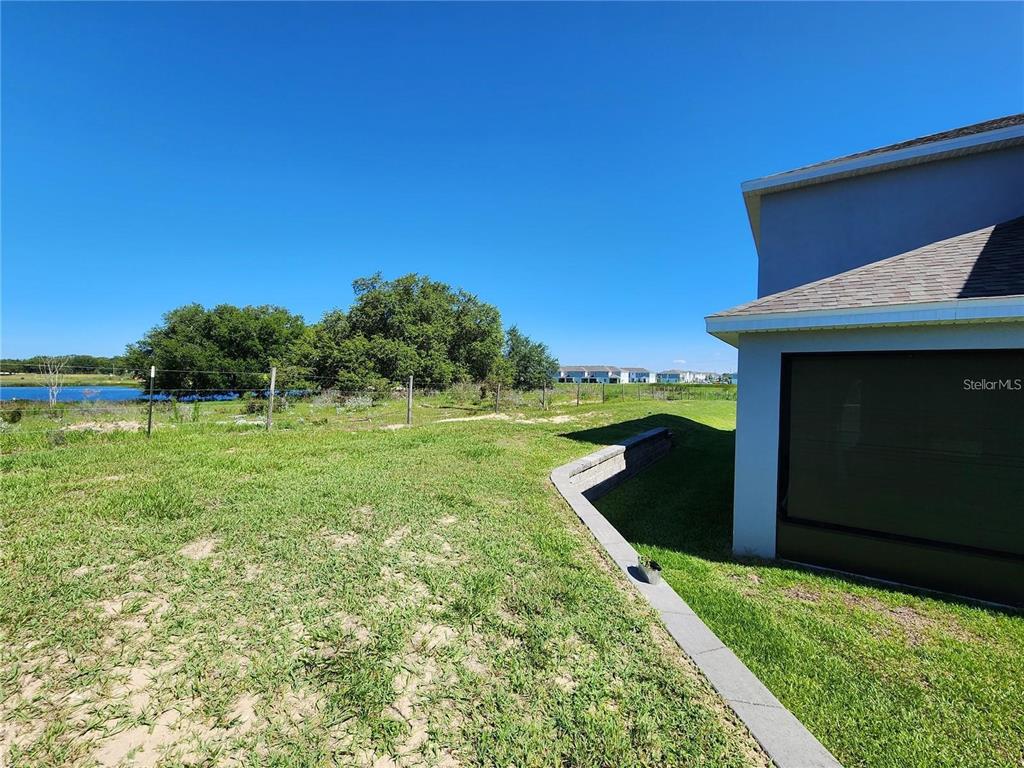 A grassy backyard features a retaining wall, a screened-in patio, and a view of a pond — 474 ANNABELLE WAY, DAVENPORT, FL