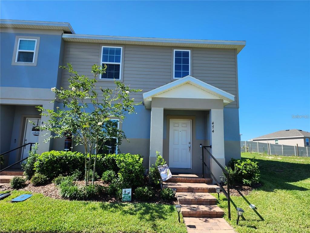 A two-story townhouse exterior features tan siding, a white front door, and a small tree — 474 ANNABELLE WAY, DAVENPORT, FL