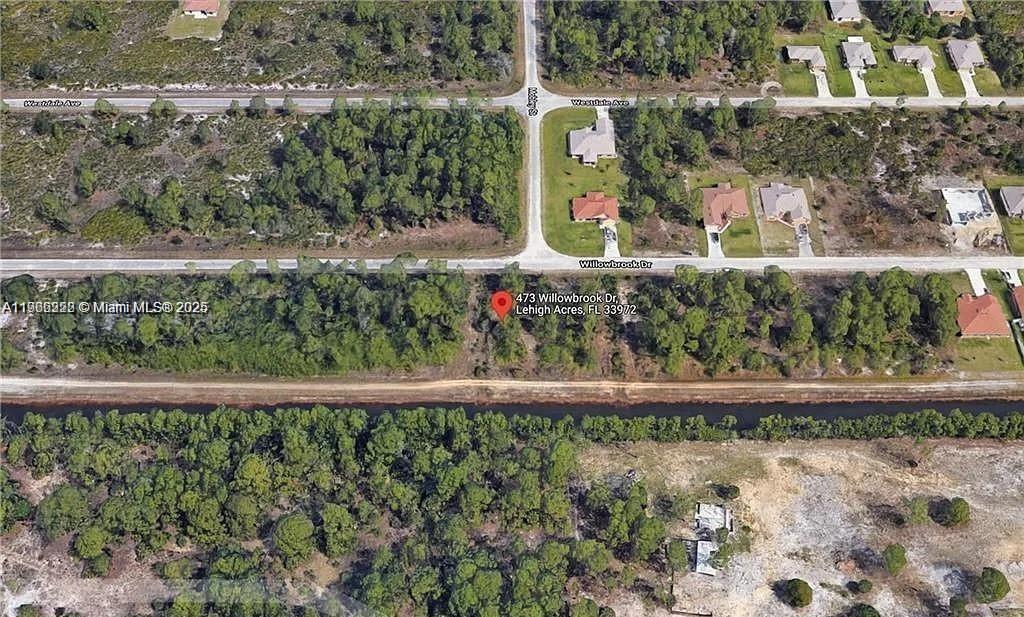 This aerial view shows a vacant residential lot located next to a canal — 473 Willowbrook Dr, Lehigh Acres FL 33972, LEHIGH ACRES, FL