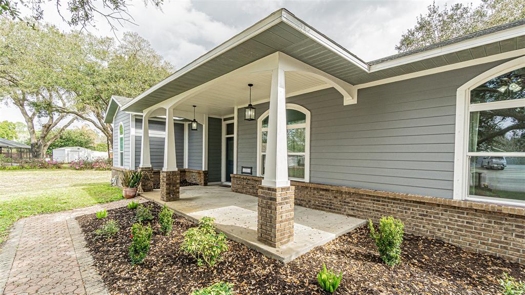 A gray-sided house features a covered front porch with brick columns and a walkway — 12211 COUNT PLACE, THONOTOSASSA, FL