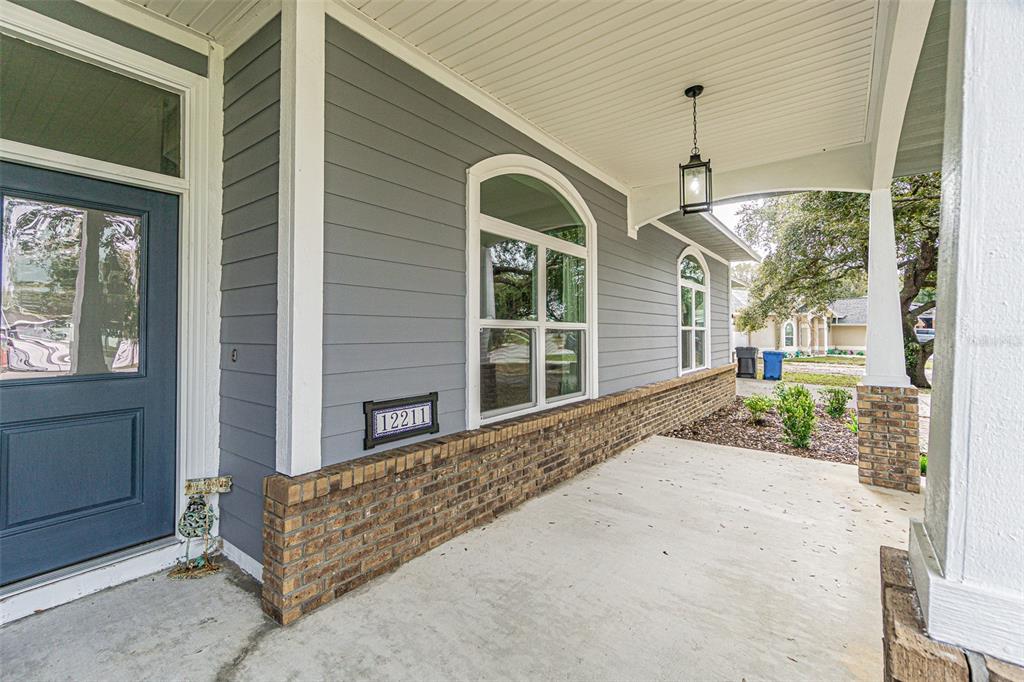 A covered front porch features gray siding, a blue door, and a brick base — 12211 COUNT PLACE, THONOTOSASSA, FL