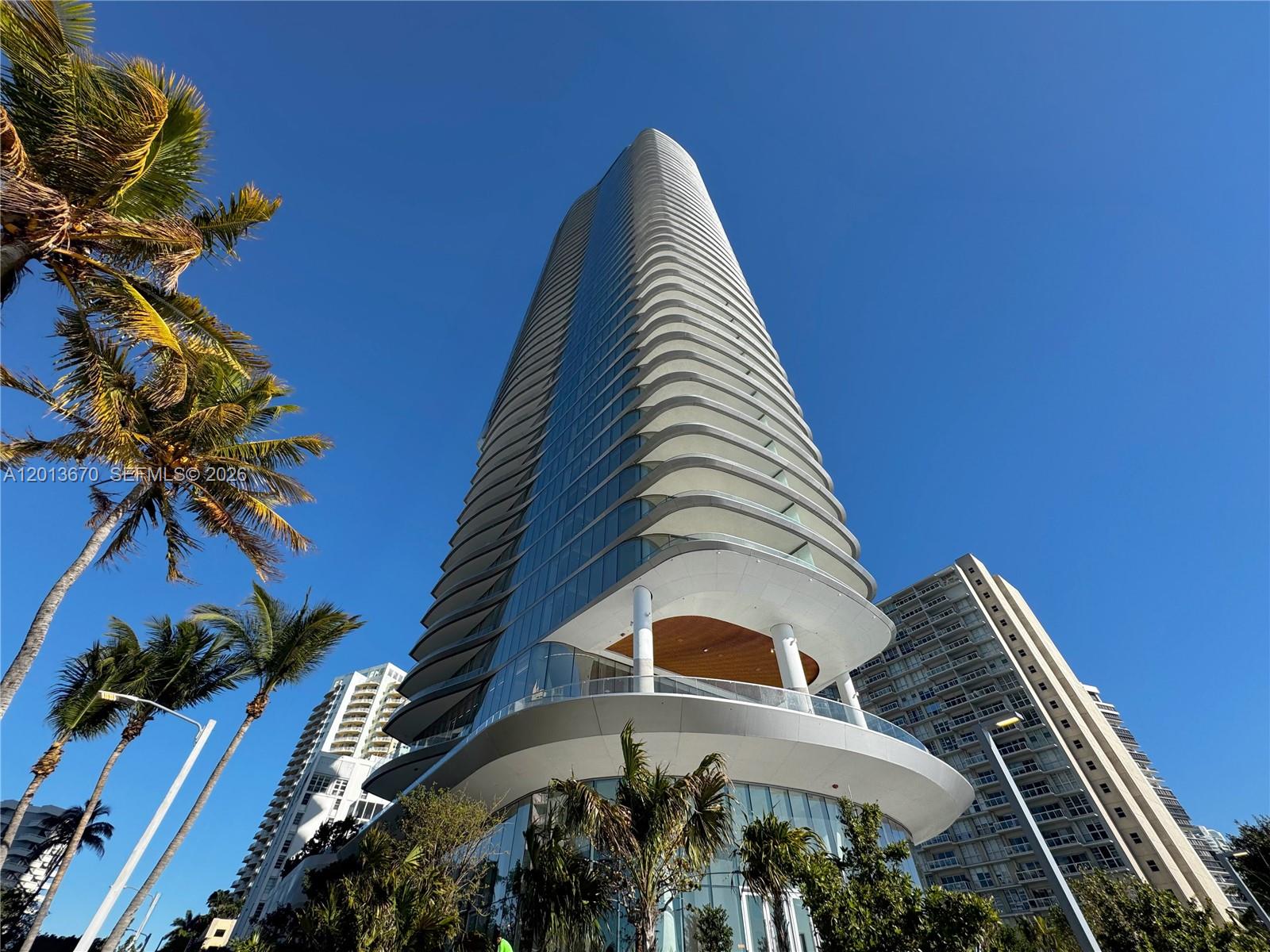 A low-angle view of a modern, curved glass skyscraper with balconies against a blue sky — 175 SE 25th Rd # 4202, Miami FL 33129, MIAMI, FL