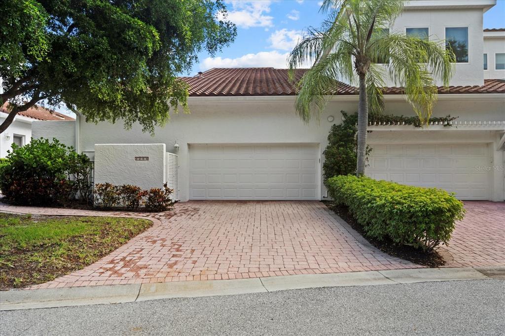 A white stucco townhouse features a two-car garage, a brick paver driveway, and a palm tree — 2254 HARBOUR COURT DRIVE, LONGBOAT KEY, FL