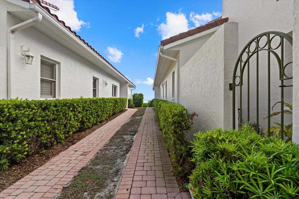 A brick walkway leads between two white stucco buildings lined with green hedges — 2254 HARBOUR COURT DRIVE, LONGBOAT KEY, FL